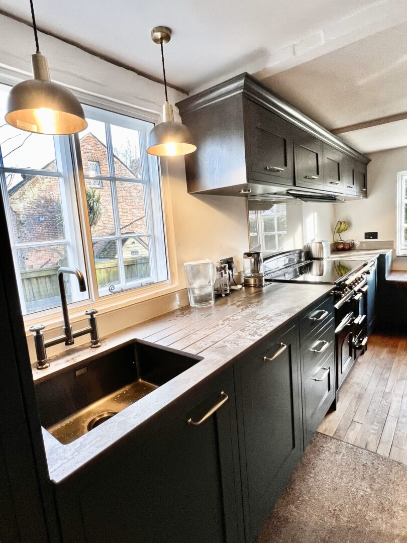 Painted Shaker style blue kitchen with Brass handles, cornice and induction Rangecooker with brass knobs, walnut effect wall units and Dekton worktops
