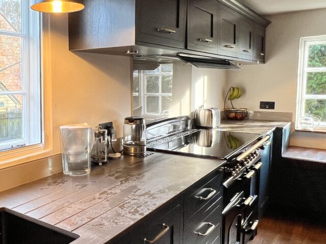 Painted Shaker style blue kitchen with Brass handles, cornice and induction Rangecooker with brass knobs, walnut effect wall units and Dekton worktops